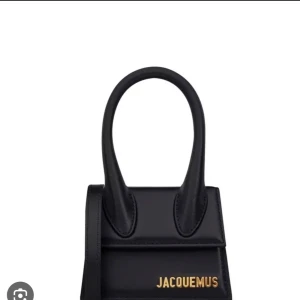 Jacquemus svart mini handväska - Superfin svart mini handväska från Jacquemus med guldiga bokstäver framtill. Väskan har ett stilrent och modernt uttryck med korta handtag och lång axelrem. Tillverkad i slätt skinn och perfekt för dig som gillar trendiga accessoarer. Skriv vid fler frågor!!!