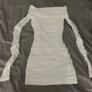 Vit offshoulder klänning Gina Tricot XS - Supersnygg vit kortklänning från Gina Tricot i storlek XS. Klänningen har offshoulder-modell, långa ärmar och är figurnära med snygga rynkade detaljer längs hela plagget. Perfekt för dig som vill sticka ut med en stilren look. Använd en gång