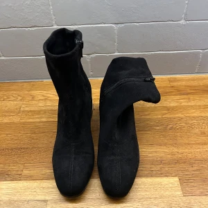 Svarta mocka stövletter med klack - Snygga svarta stövletter i mocka från Tamaris med rund tå och stabil blockklack. Skorna har dragkedja på insidan för enkel påtagning och en stilren, minimalistisk look. Perfekta till både jeans och kjol för en trendig vibe.