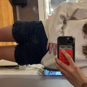 Mörkblå spetsiga shorts med volang - Säljer ett par mörkblå shorts med snygga spetsdetaljer och volangkant. De är högmidjade och har en feminin look med broderade blommor och struktur. Perfekta för sommarens alla tillfällen när du vill sticka ut lite extra. Den har två hål vid spetsen men det är ingenting man ser. 
