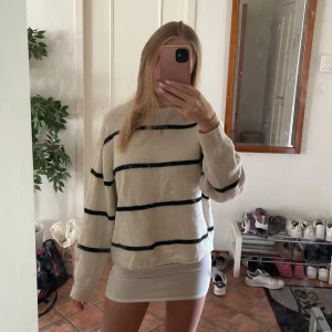 Randig stickad tröja  - Kräm vit stickad tröja med svarta horisontella ränder. Tröjan har en loose passform, rund halsringning och långa ärmar. Perfekt inför kyliga sommarkvällar!