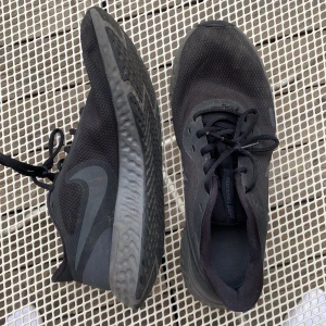 Svarta Nike Revolution löparskor - Svarta Nike Revolution sneakers med mesh-ovandel och klassisk swoosh på sidan. Skorna har snörning, platt sula med vågigt mönster och är perfekta för löpning eller vardag. Lätta och andas bra, stilrena och sportiga för dig som gillar en clean look. Är använda och pris kan diskuteras!