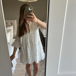 Vit kort klänning med volang - Superfin vit kortklänning med broderade detaljer och volanger. Klänningen har trekvartsärm med volangkant och v-ringning. Lätt och luftig modell som ger en romantisk vibe, perfekt för varma dagar.