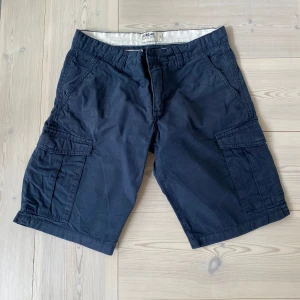 Mörkblå cargoshorts från Gabbet - Snygga mörkblå cargoshorts från Gabbet med flera praktiska fickor på sidorna och bak. Klassisk passform och robust bomullsmaterial som passar perfekt till sommaren. 