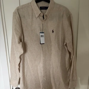 Beige Polo Raulph Lauren Linné skjorta  - Skön linne skjorta från Polo Raulph Lauren som aldrig är använd, sjukt nice material och lappen är fortfarande kvar. Riktigt fräsch till sommaren, skriv gärna om mer frågor, pris är ej spikat! QR kod finns även innanför som leder till raulph laurens hemsida.