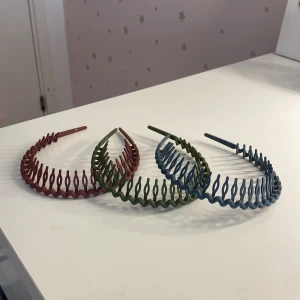 Tre vågiga diadem i olika färger - Säljer tre coola diadem i vågig design, perfekta för att hålla håret på plats. Ett är matt rött, ett matt grönt och ett matt blått. De är gjorda i plast och har en unik, öppen struktur som ger en trendig look. Passar dig som vill sticka ut med accessoarer.