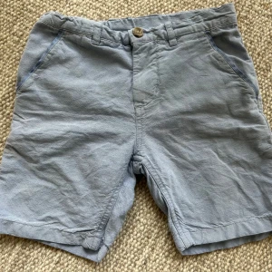 Ljusblå bomullsshorts Polarn O. Pyret - Ljusblå shorts från Polarn O. Pyret i mjuk bomull med normal passform. Klassisk design med knapp och dragkedja framtill, hällor för bälte och fickor både fram och bak. Perfekta för varma dagar och enkel att matcha med t-shirt eller skjorta.