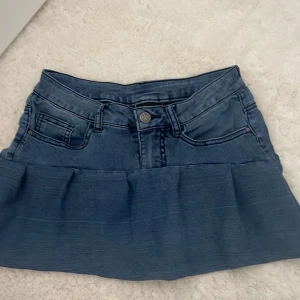 Blå jeanskjol, stl xs - Snygg blå jeanskjol i kort modell med klassiska fickor fram och bak, bälteshällor och knappstängning. Perfekt för dig som gillar en avslappnad och trendig stil. Passar till allt från sneakers till boots.