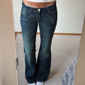 Mörkblå bootcut jeans från Weekday - Snygga mörkblå jeans från Weekday med bootcut passform och klassisk femficksdesign. Jeansen har en lätt tvättad look med slitningar framtill och bakfickor med Weekday-logga. Perfekta för dig som gillar en retro vibe och vill ha ett par jeans med lite vidare ben. Midja: 37 cm (rakt över), 46 cm (rakt över) och innerbenslängd: 83 cm. Jeansen är i Style: Nova Low Slim Bootcut Jeans och i storlek W27 L34. Varan är använd ett fåtal gånger!