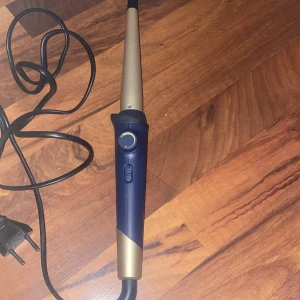 Remington locktång med fodral - Remington locktång i snygg blå och guldig design. Konformad stav för naturliga lockar, med sladd och på/av-knapp. Kommer med ett svart fodral med Remington-logga. Perfekt för att fixa snygga lockar snabbt och enkelt. Den var köpt i slutet av april 2025 och har blivit använd 2 gånger för jag insåg att lockigt hår inte passar mig och jag köpte den för 500kr och jag har kvar kartongen 