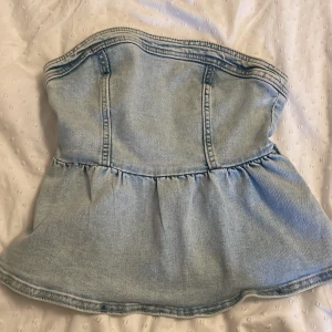 Ljusblå jeanskorsett från H&M XS - Supersnygg ljusblå jeanskorsett från H&M i storlek XS. Axelbandslös bandeau-modell med markerade sömmar, volang nertill och dragkedja bak. Perfekt för dig som vill ha en trendig och edgy look med denim vibes.