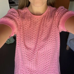 Rosa blus  - Supersöt rosa blus med korta ärmar och puff vid axlarna. Toppen har ett genomgående hålmönster och ribbade muddar i ärmslut och halsringning. 