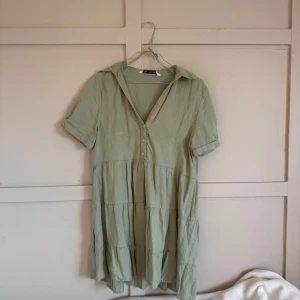 Ljusgrön kort klänning från Zara - Superfin ljusgrön klänning från Zara i luftig bomull/linne-blandning. Den har korta ärmar, v-ringning med knappar och volangiga lager. Perfekt för varma dagar och enkel att styla med sneakers eller sandaler.