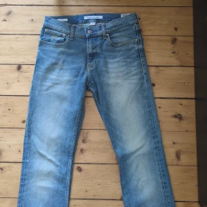 Blå jeans från Calvin Klein W28 L34 - Snygga blå jeans från Calvin Klein med klassisk femficksdesign och ljusa slitningar framtill. Jeansen har raka ben och normal passform, tillverkade i bomull med Calvin Klein-logga på knappen och bakfickan. Perfekta för en avslappnad stil.
