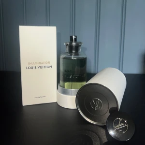 Louis Vuitton Imagination Parfym - Lyxig parfym från Louis Vuitton, Imagination Eau de Parfum. Flaskan är genomskinlig med svart lock och silverdetaljer, och parfymen har en ljusgrön nyans. Kommer i elegant vit kartong och rund förvaringsask med LV-logga. Perfekt för dig som gillar exklusiva dofter.