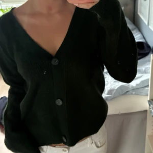 Grön stickad kofta med v-ringning - Mysig grön stickad kofta med djup v-ringning och stora knappar framtill. Koftan har långärmad passform och en lite loose fit, perfekt att slänga på sig över en t-shirt eller linne.