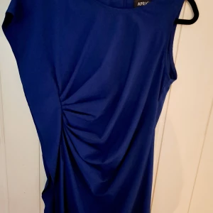 Så snygg på! - Snygg kornblå klänning från Apricot i storlek S/M. Klänningen är ärmlös med rund halsringning och har en cool rynkad detalj i sidan som ger en schysst form. Perfekt för dig som gillar stilrena plagg med en twist.Så snygg figursydd blå klänning med en sido volang fall, sitter tightish och är relativt kort i modellen. Super snygg på!