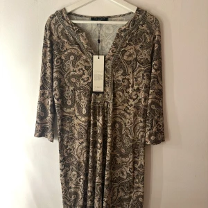 Ilse Jacobsen klänning  - Elegant klänning från Ilse Jacobsen i ett vackert paisley-mönster. Klänningen har en V-ringning med dekorativa detaljer. Perfekt för både vardag och fest. Storlek M. Nypris 1800kr. Ny med prislapp