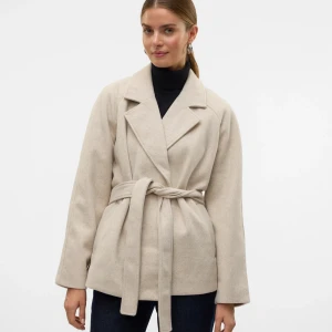 Beige kappa med bälte och krage - Stilren beige kappa med bred krage och knytskärp i midjan. Jackan har lång ärm och en klassisk, rak passform som ger en clean look. Perfekt att slänga över en polotröja för en snygg och enkel outfit. Använd få antal gånger. Xs men sitter som s