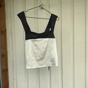 Svartvit omlott korsett-topp - Snygg svartvit topp med breda axelband och knytning i ryggen. Toppen har en cool kontrast mellan svart upptill och vitt nedtill, och knytdetaljen bak ger en unik look. Perfekt för dig som vill sticka ut med en trendig och stilren topp.