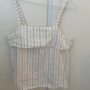Randig linnetopp från H&M, beige/vit - Säljer en luftig linnetopp från H&M i storlek S. Toppen är vit med tunna beigea ränder, har smala justerbara axelband och dragkedja på baksidan. Perfekt för varma dagar med sin lätta bomullskänsla och avslappnade passform.