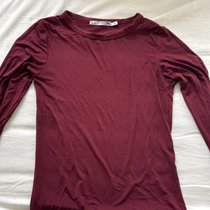 Vinröd långärmad tröja från 157 - En enkel och stilren vinröd långärmad tröja från 157 i mjuk bomull. Tröjan har rund halsringning och en slim passform som sitter snyggt på kroppen. Perfekt att matcha med jeans eller kjol för en clean look.