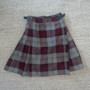 Rutig kilt  - Svinsnygg knälång kilt med omlottstängning och spännen i sidorna! Tartanrutig i grå och röd med slät framsida och veckad baksida 🫶🏻storlek W25 💕Köpt på beyond retro. 🫶🏻