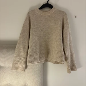 Beige stickad tröja med ribbade detaljer - Mysig beige stickad tröja med rund halsringning och breda ribbade muddar vid ärmslut och nederkant. Perfekt för lager-på-lager och chill dagar. Enkel och stilren design som passar till det mesta.