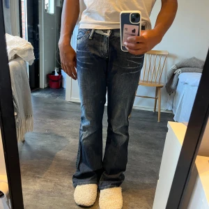 Blå bootcut jeans från Take Two - Säljer ett par blå jeans från Take Two med bootcut passform och snygga slitningar. Jeansen har klassisk femficksdesign, kontrastsömmar och läderpatch bak i midjan. Materialet är robust denim i bomull och de har låg midja för en avslappnad vibe.