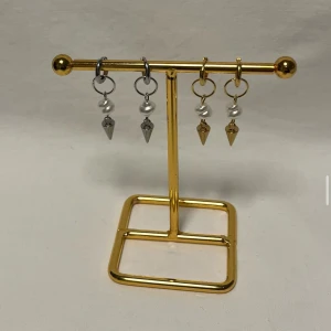 Örhängen med pärlor och konhängen - Säljer fyra par örhängen med cool design – två i silverfärg och två i guld. Alla har en vit pärla och en konformad hängande detalj. Perfekt för dig som gillar att mixa metaller och vill ha något unikt till öronen.