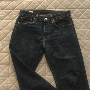 Levi's 501 mörkblå jeans W31 L30 - Klassiska Levi's 501 jeans i mörkblå denim med raka ben och snygga kontrastsömmar. Modellen har fem fickor, knappgylf och den ikoniska läderpatchen bak i midjan. Perfekta för dig som gillar tidlös stil och schysst passform.
