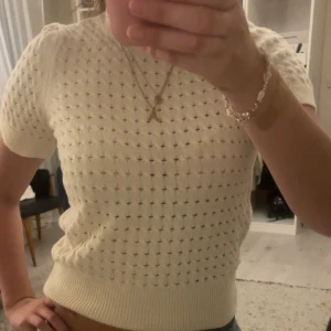Vit stickad kortärmad tröja - Supersöt vit/beige stickad tröja med korta ärmar och hålmönster över hela. Tröjan har ribbade muddar vid hals, ärmslut och midja. Perfekt till jeans eller kjol för en fräsch och trendig look.