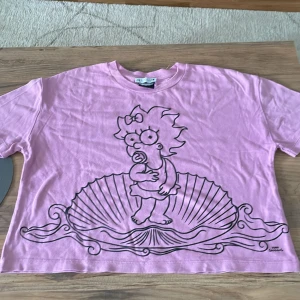 Rosa Maggie Simpson t-shirt - Säljer en rosa t-shirt från Zara med en stor svart tecknad print av Maggie Simpson på framsidan. T-shirten har korta ärmar, rund hals och är i mjuk bomull. ä