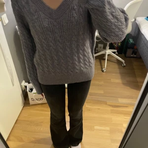 Grå stickad tröja med v-ringning - Mysig grå stickad tröja med v-ringad hals och långa ärmar. Tröjan har ett klassiskt flätmönster och breda ribbade muddar vid ärmslut och nederkant. Perfekt för lager-på-lager och chill höst- eller vinterstil. Helt ny aldrig använt den!