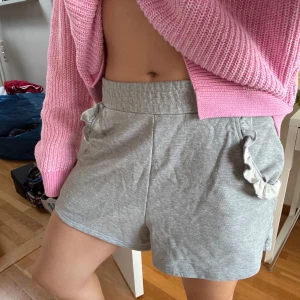 Grå bomullsshorts från & Other Stories - Supermjuka grå shorts från & Other Stories i 100% bomull. De har elastisk midja, normal passform och söta volangdetaljer vid fickorna. Perfekta för chill dagar eller när du vill vara bekväm men ändå söt.