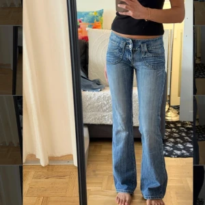 Blå bootcut jeans med låg midja - Säljer ett par blå jeans med låg midja och bootcut-modell. Jeansen har snygga detaljer som stora fickor både fram och bak samt en liten dragkedja på ena bakfickan. Klassisk tvättad denim med markerade sömmar och avslappnad passform.