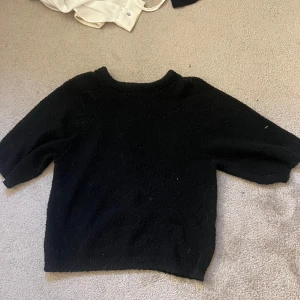 Svart stickad T-shirt från Lindex XS - Mysig svart stickad tröja från Lindex i storlek XS. Tröjan har en enkel design med rund halsringning och lite kortare ärmar, perfekt för lager-på-lager under höst och vinter. Passar dig som gillar en basic och stilren look. Använd fåtal gånger.