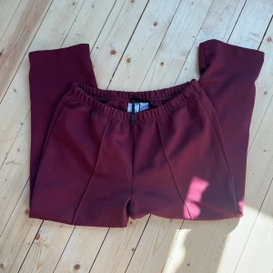 Vinröda mjukisbyxor med resårmidja - Mysiga vinröda mjukisbyxor i 100% polyester med resår i midjan och snörning. Byxorna har en relaxed fit och är perfekta för chill dagar. Tjockare material och stilrena sömmar framtill ger en snygg look.