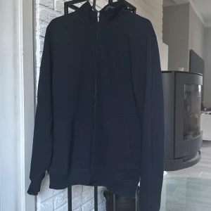 Mörkblå zipjacka från Dressmann - Mörkblå jacka från Dressmann med hel dragkedja framtill och två fickor. Jackan har en enkel, clean look med hög krage och är tillverkad i mjukt material. Perfekt för dig som gillar stilren och bekväm vardagsstil.