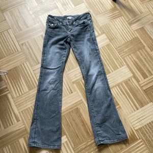 Grå bootcut jeans med fickdetaljer - (Ord pris 359kr) (använda en gång) Snygga grå jeans med bootcut passform och markerade sömmar. Byxorna har coola fickor med lock och silverknappar både fram och bak. Perfekta för dig som gillar en avslappnad men trendig look.