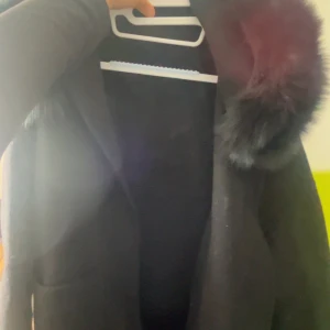 Svart kappa med päls på huvan - Snygg svart kappa med stor huva kantad av fluffig fuskpäls. Jackan har en rak och stilren passform, perfekt för kalla dagar. Materialet känns mjukt och värmande, och designen är enkel men ändå lyxig. Passar dig som vill ha en klassisk look med en twist.Skriv privat för bild på,Köptes för 1000kr säljer även på Vinted. 