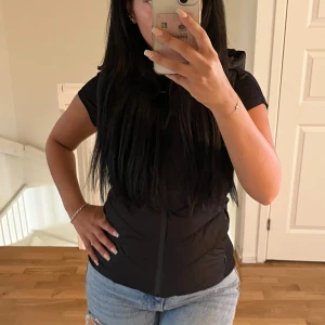 Svart dunväst med huva - Säljer en svart dunväst med dragkedja framtill och praktisk huva med dragsko. Västen har en tight passform. Använd max 2 gånger så i väldigt bra skick.