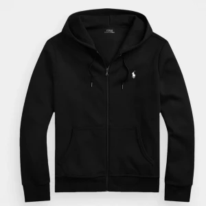 Svart hoodie från Polo Ralph Lauren - Råkade köpa 2 och säljer av enSvart hoodie från Polo Ralph Lauren med dragkedja framtill, huva med snörning och klassisk vit logga på bröstet. Tröjan har känguruficka och är tillverkad i mjuk bomull. Perfekt för en chill och stilren look.