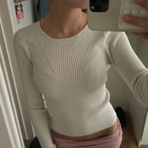 Vit ribbad stickad tröja - Säljer en vit, ribbad stickad tröja med lång ärm och rund hals. Tröjan har en tight passform och är stretchig, vilket gör den riktigt skön och smickrande. Perfekt att styla med jeans eller kjol för en clean look.