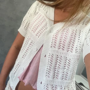 Vit stickad kofta med kort ärm - Superfin vit stickad kofta med korta ärmar och v-ringning. Koftan har ett genomgående hålmönster och knäpps med knappar framtill. Perfekt att slänga över ett linne eller klänning för en fräsch och somrig look.