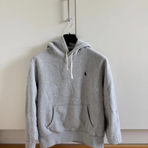 Grå hoodie från Polo Ralph Lauren - Snygg grå hoodie från Polo Ralph Lauren med klassisk broderad logga på bröstet. Tröjan har huva med vita snören, känguruficka och mjukt material på insidan. Perfekt för chill dagar och enkel att matcha med jeans eller mer chill outfits. Strl M men passar bäst S. PRISET ÄR FÖRHANDLINGSBART!