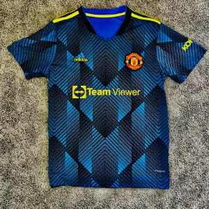 Manchester United Rashford 10 bortatröja - Snygg Manchester United bortatröja från Adidas med Rashford 10 på ryggen. Tröjan är blå med svarta och ljusblå grafiska mönster, gula sponsorer och klubbmärke på bröstet. Tillverkad i lätt och ventilerande Aeroready-material. Perfekt för dig som vill sticka ut på läktaren eller planen.