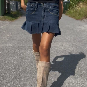 Mörkblå jeanskjol med volangkant - Supersnygg mörkblå jeanskjol med volangkant nertill och låg midja. Kjolen är kort och har en cool denimkänsla. Var tidigare jeansbyxor, men omsydd till kjol för en mer trending och unik look så att den kan komma till användning igen. Snyggt, billigt och miljövänligt. 