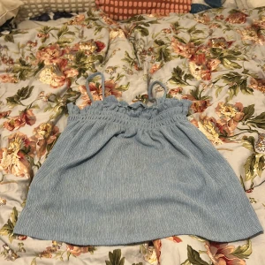 Ljusblå linnetopp från Gina Tricot - Supersöt ljusblå linnetopp från Gina Tricot med smockad överdel och tunna axelband. Toppen har en avslappnad passform och är perfekt för varma dagar. Materialet är mjukt och lätt, vilket gör den extra skön att bära.