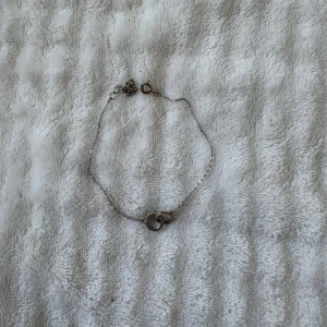 Silverfärgat armband med två ringar - Ett tunt och stilrent armband i silverfärg med två sammanlänkade ringar i mitten, varav en är dekorerad med små stenar. Perfekt för dig som gillar minimalistiska smycken med en twist.